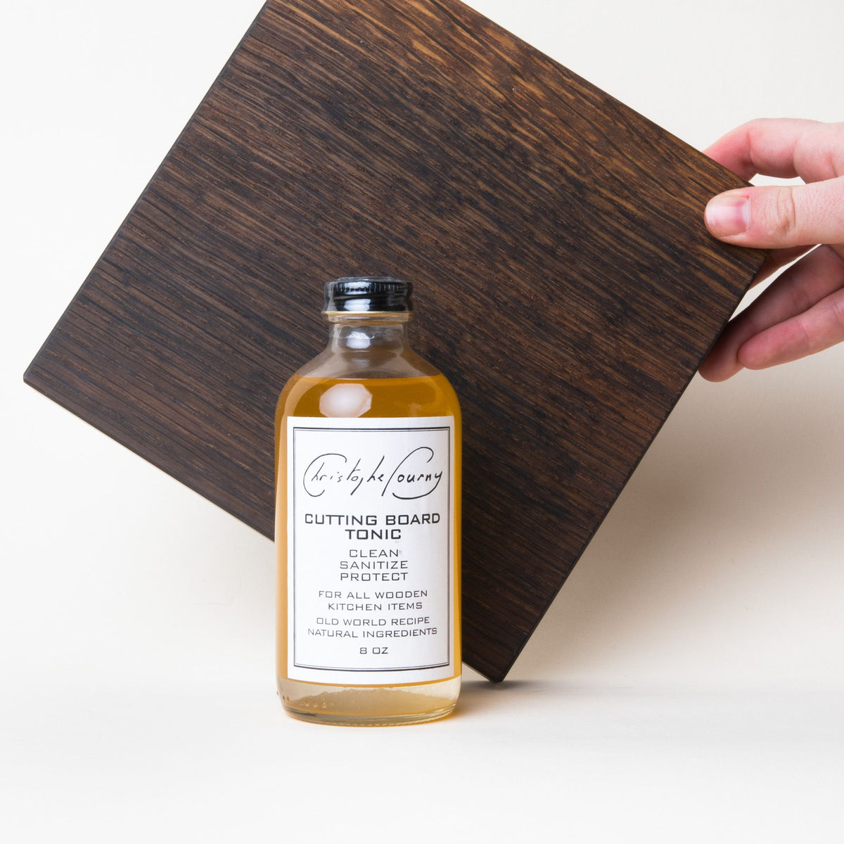 Glass bottle with a black screw top and a white label that reads "Cutting Board Tonic", in front of a dark wood cutting board
