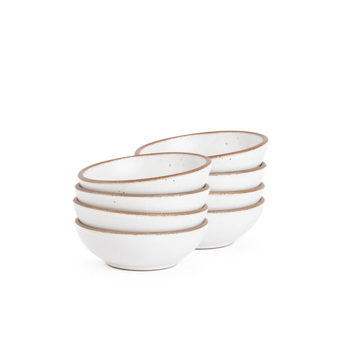 A stack of 8 small shallow ceramic bowls in a cool white color featuring iron speckles and an unglazed rim