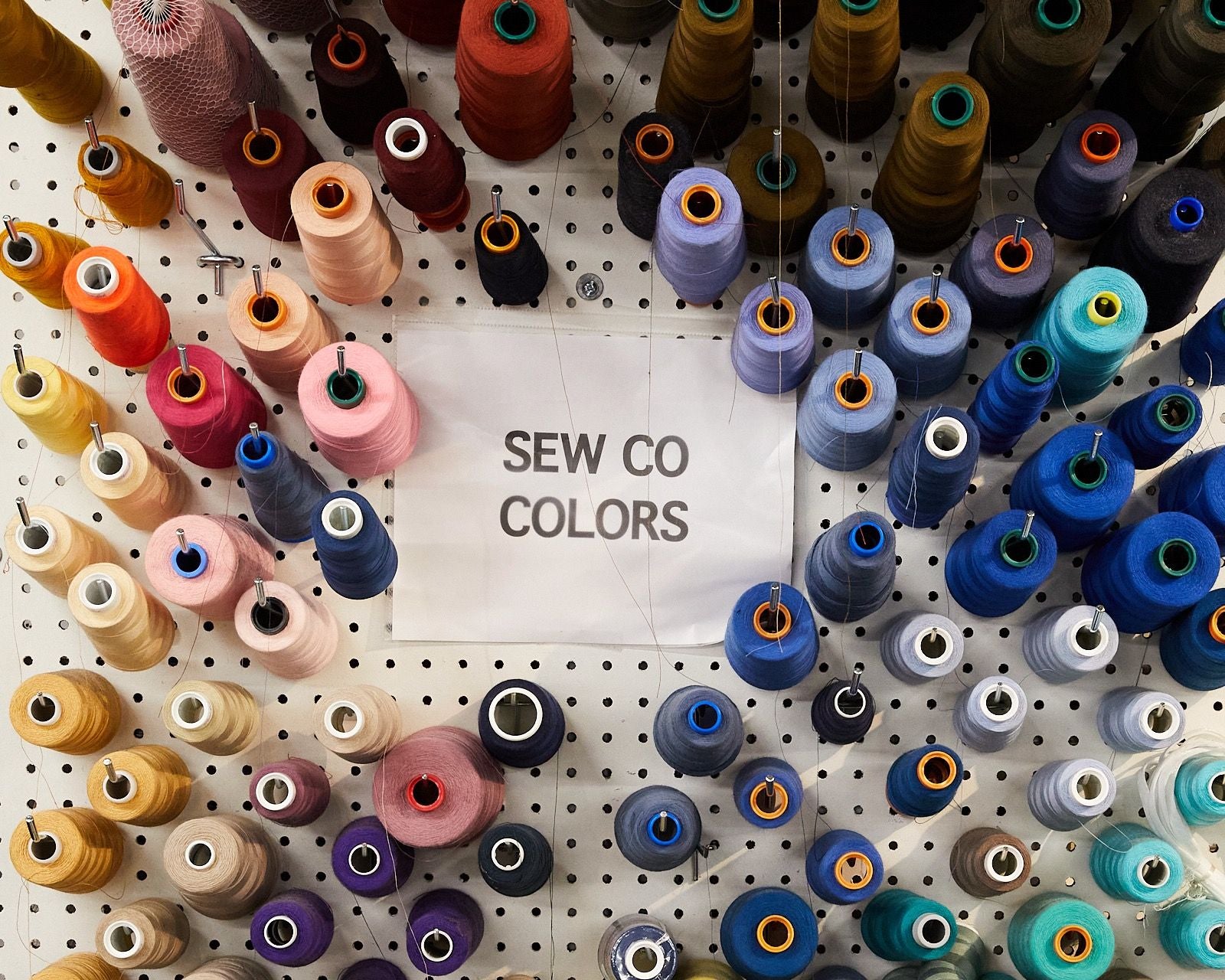 A peg wall filled with large spools of colorful thread and a sign that reads