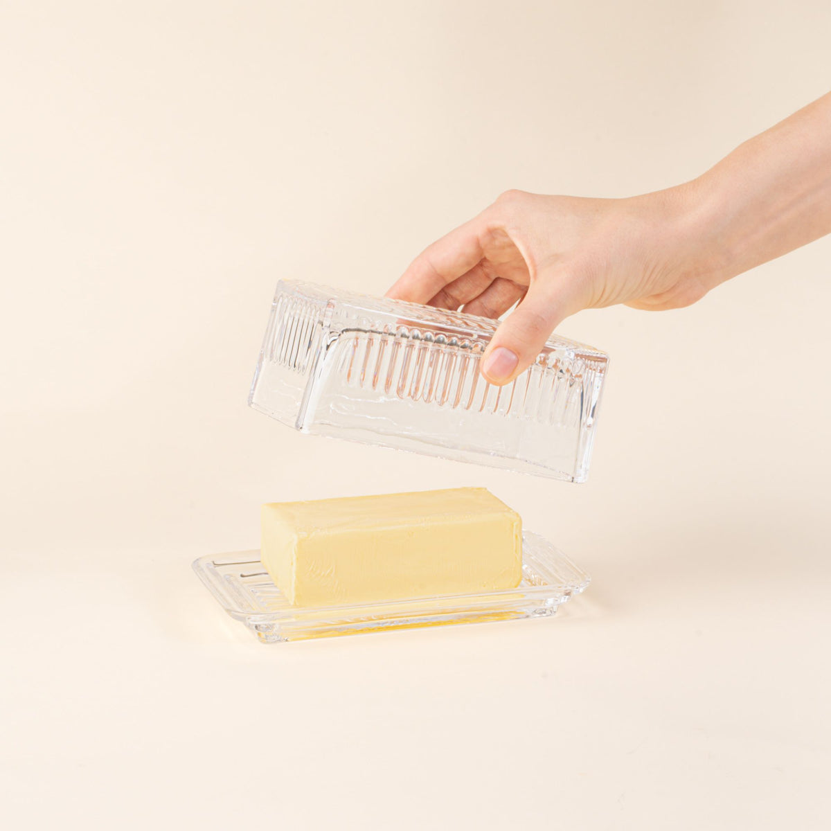 Hand holds a lid over a glass butter dish with butter on top