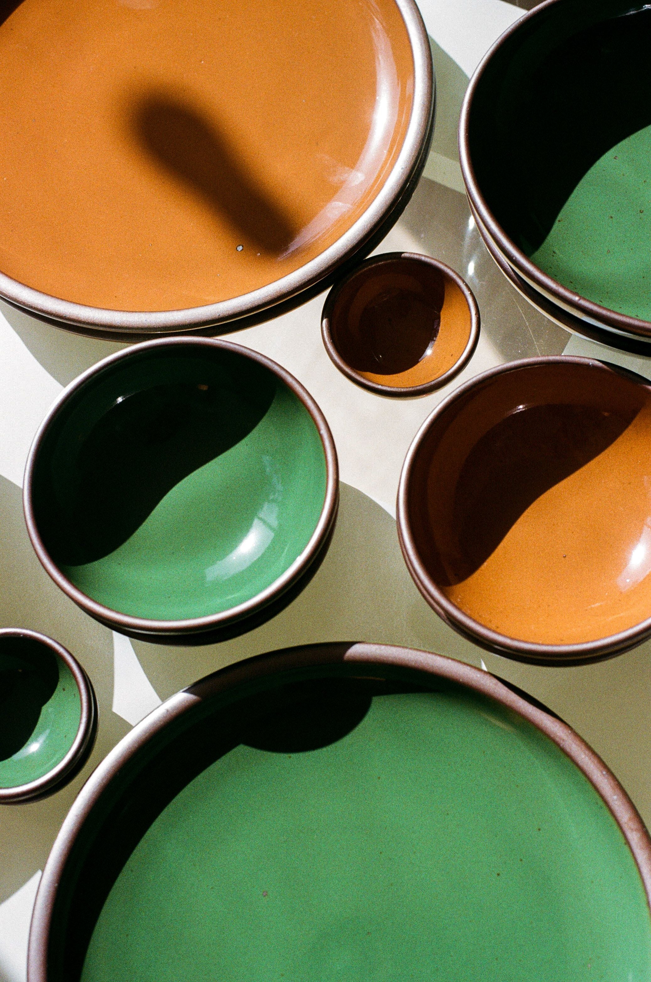 Shiny green and brown pots in direct sun on. a white background with high contrast shadows.