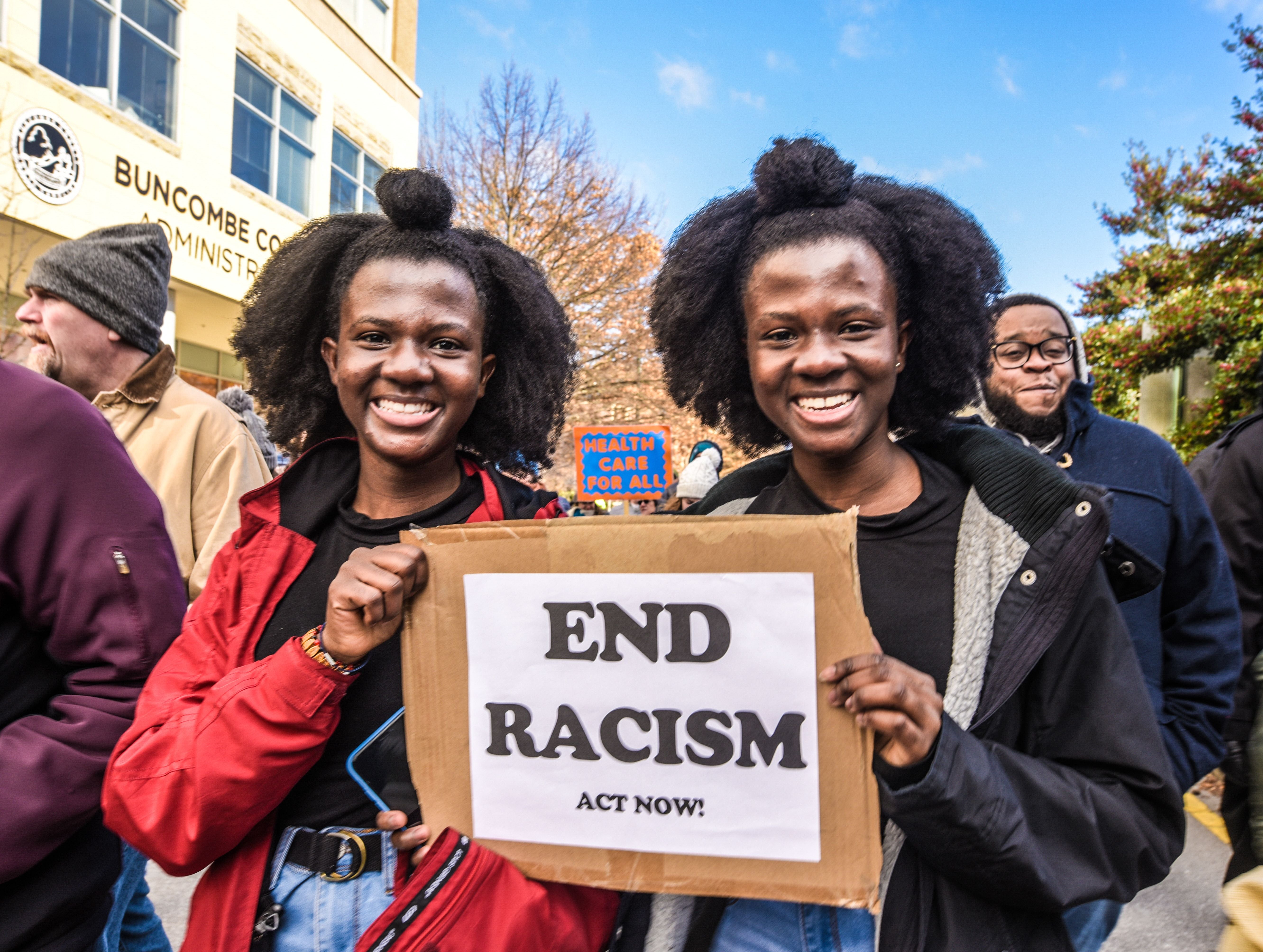 Twins are outside in a march and sharing a sign they both are holding that reads