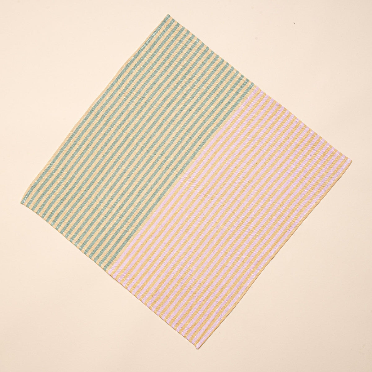 A square napkin that is half striped green and peach, the other half is striped pink and peach.