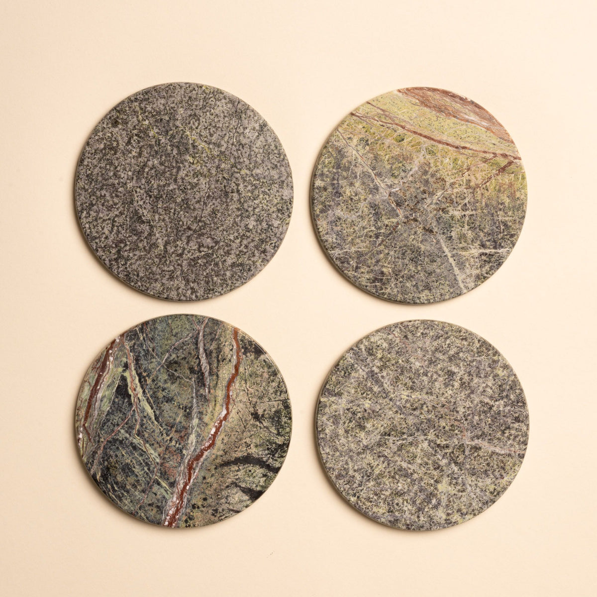 Set of four round stone coasters in varied earthy tones of green, gray, and rust with natural veining patterns.