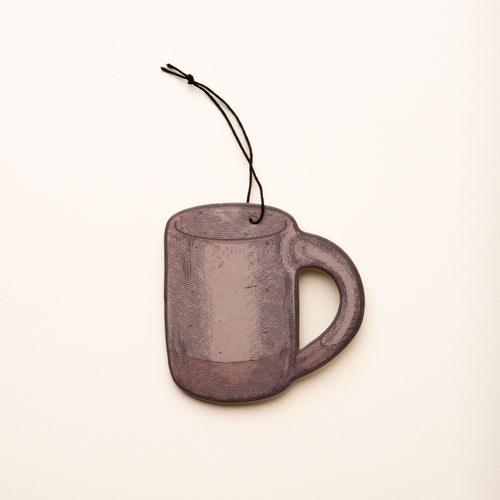 Illustrated mug-shaped air freshener in a pale warm brown color with a black hanging string against a light cream background.