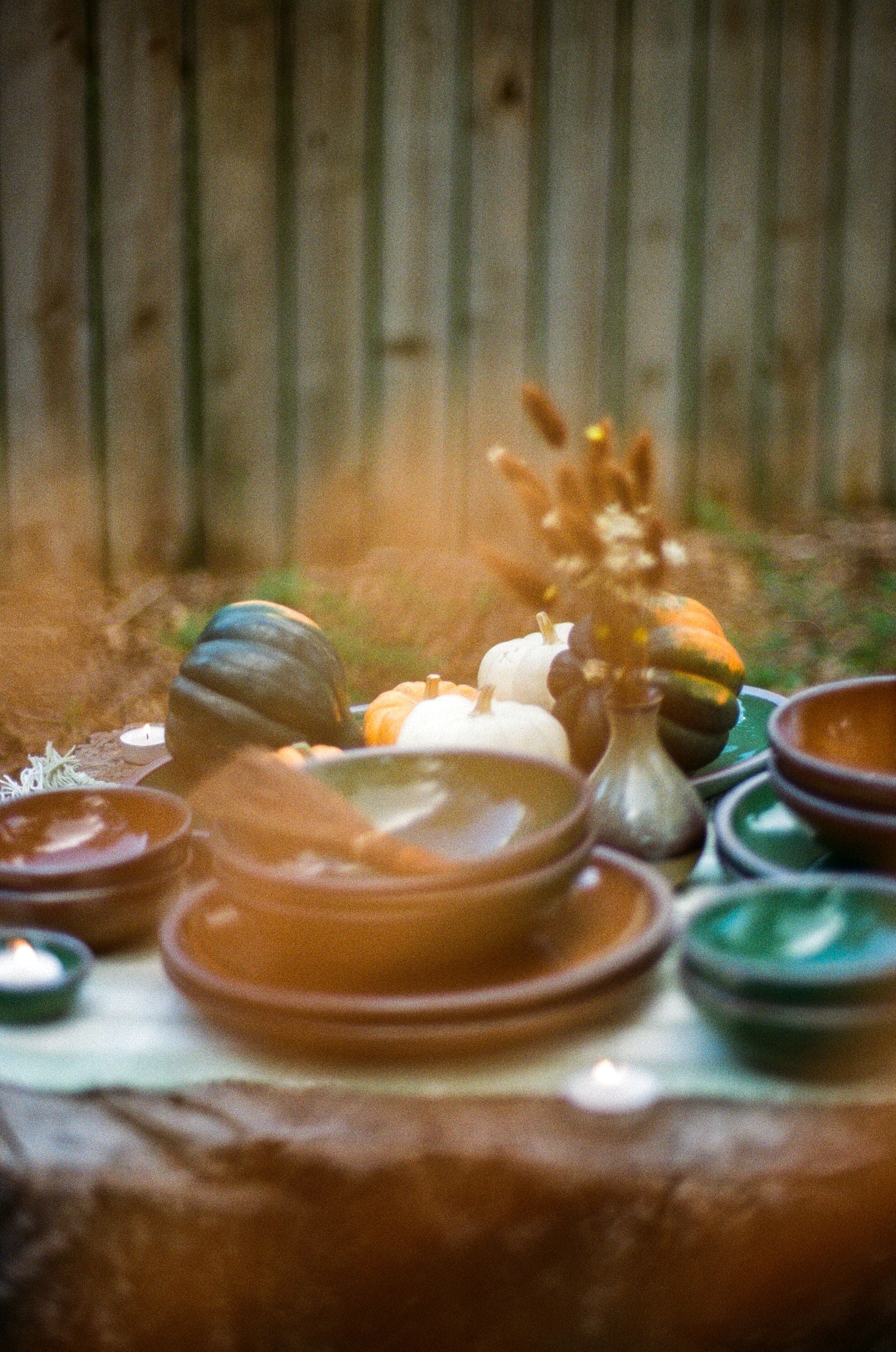 Shiny green and brown pots sit outside on a stump topped with small gourds and dried florals.