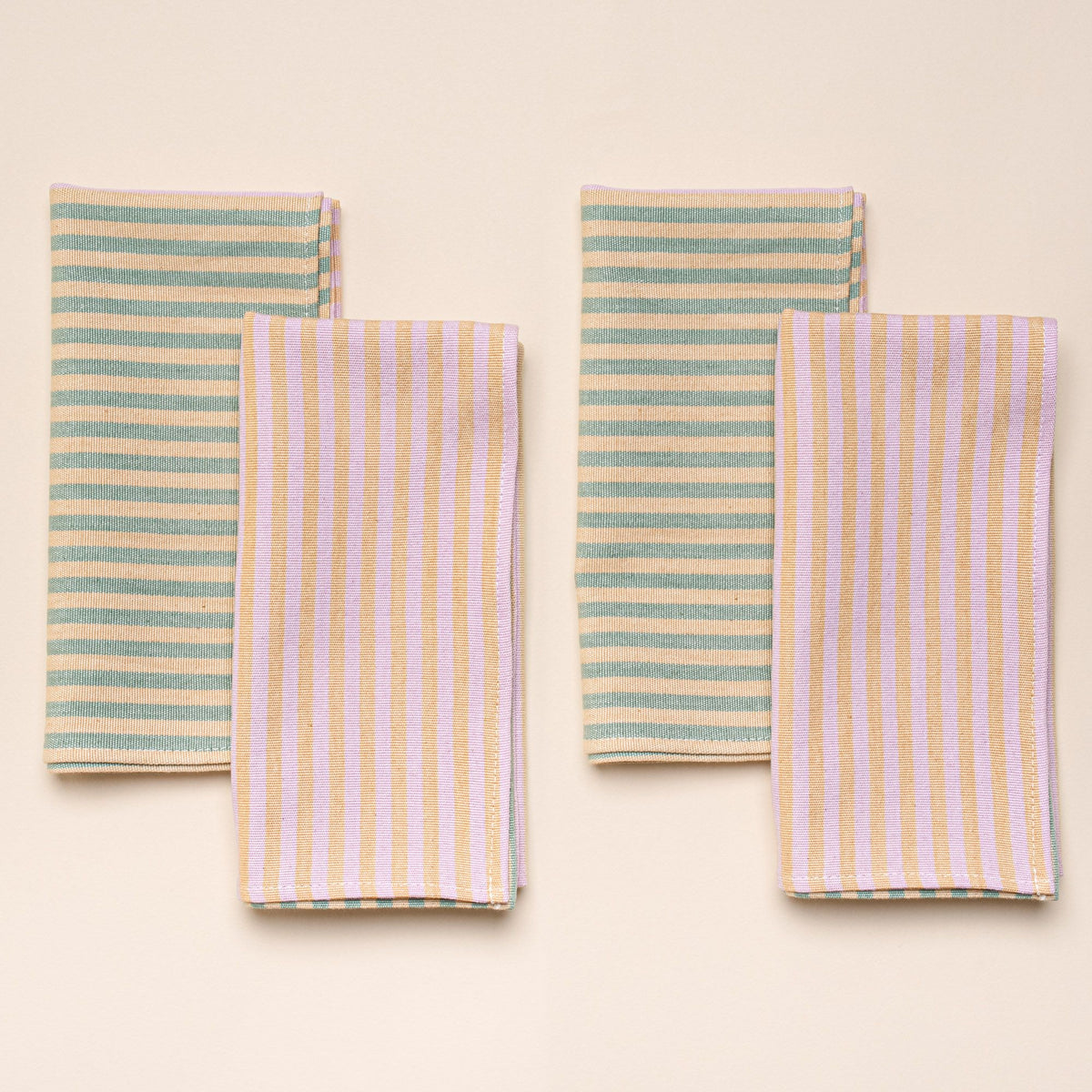 4 folded napkins featuring color blocks of striped peach and pink, and striped peach and green.