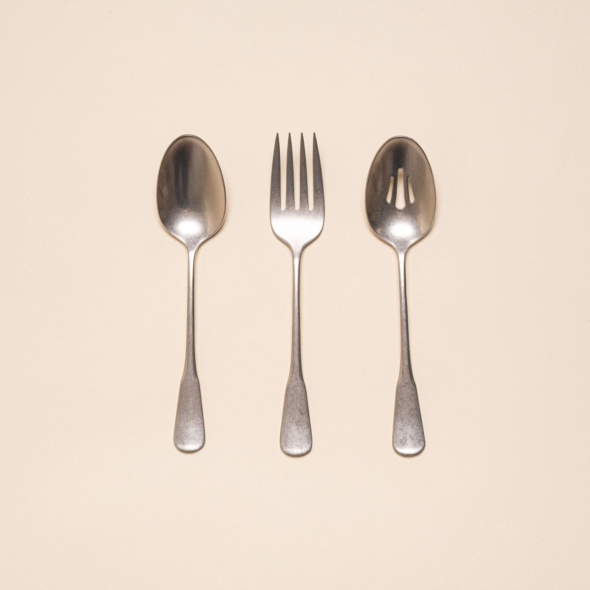 Three stainless steel serving utensils including a serving fork, serving spoon, and pierced spoon in a tumbled matte finish with a classic design.
