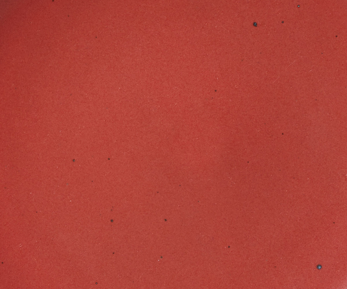 A closeup of a ceramic plate in a deep red color with iron speckles throughout