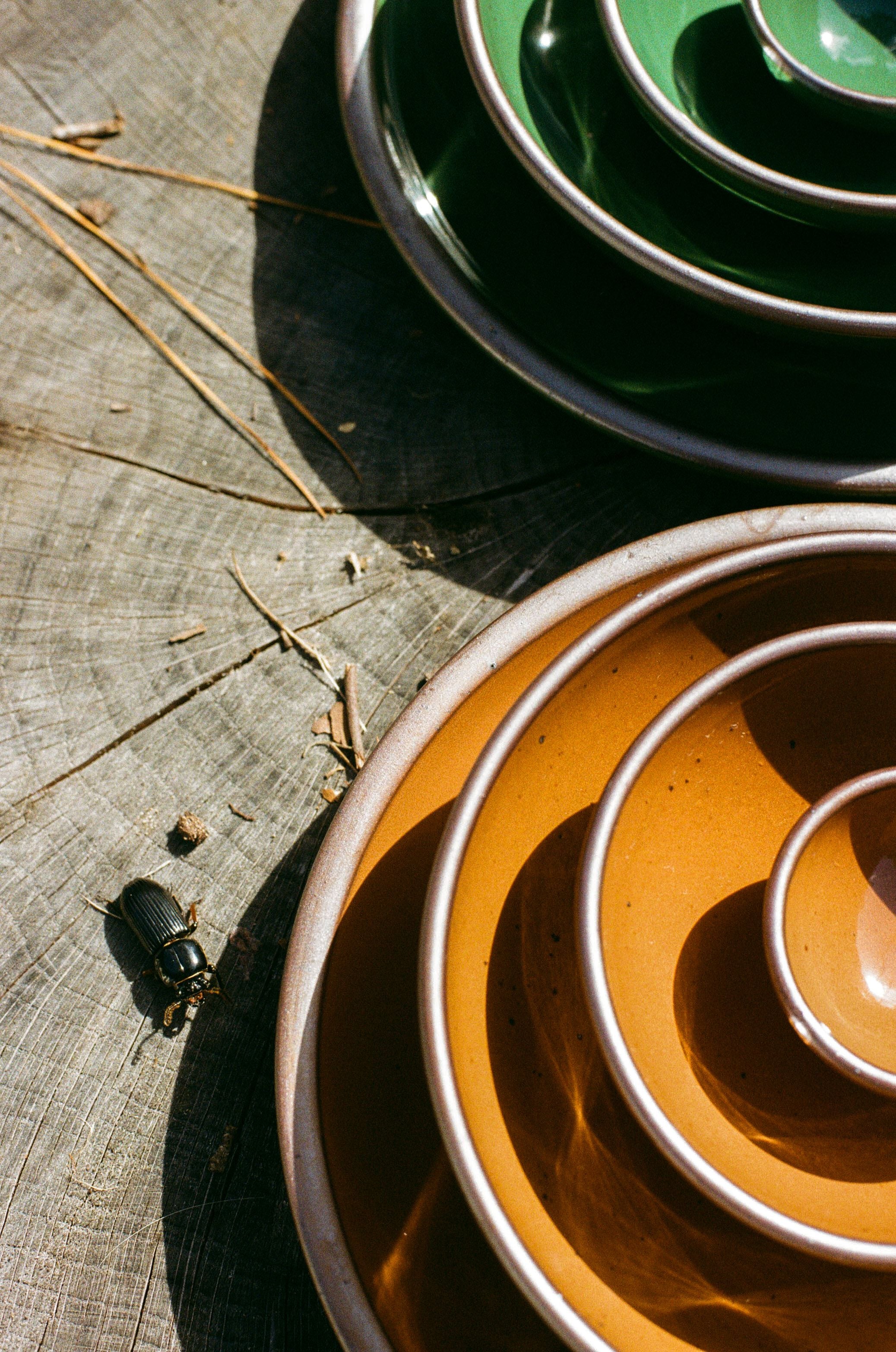 Stacks of shiny green and brown pots sit on a stump next to a black beetle.
