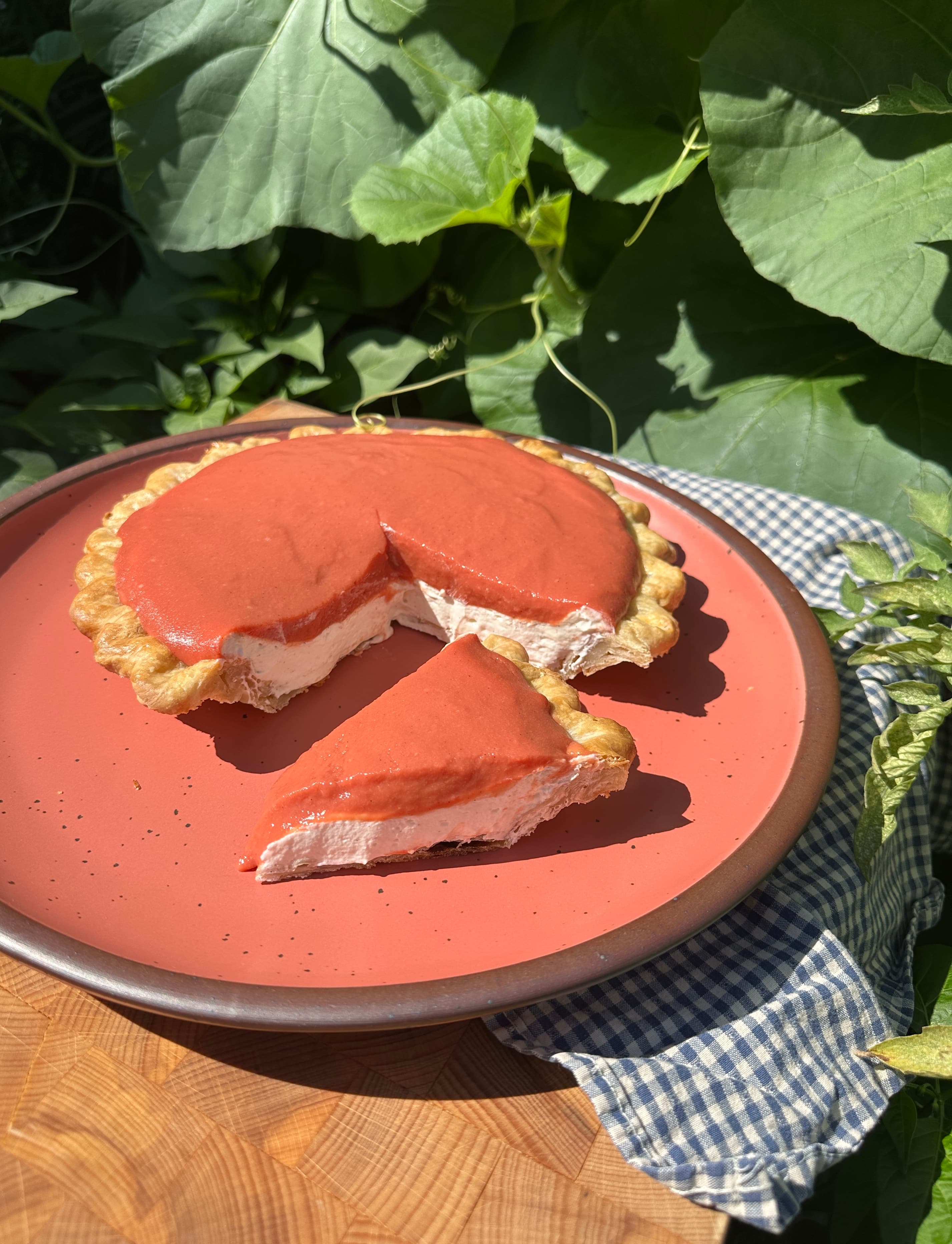 Slice of pie with whipped filling and guava topping on a coral plate, with greenery in the background.