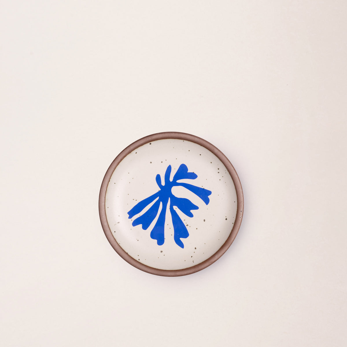 A ceramic dessert sized plates in a warm off-white color with unglazed rim, a frond-like cut-outs from Henri Matisse’s La Perruche et la sirène.