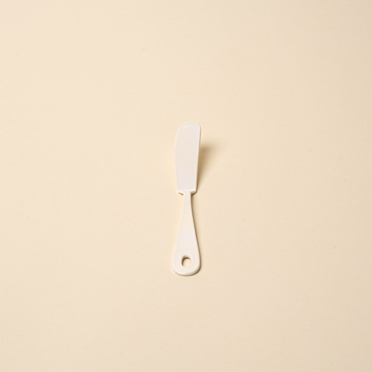 A white enamel butter knife with a hole at the end of the handle.