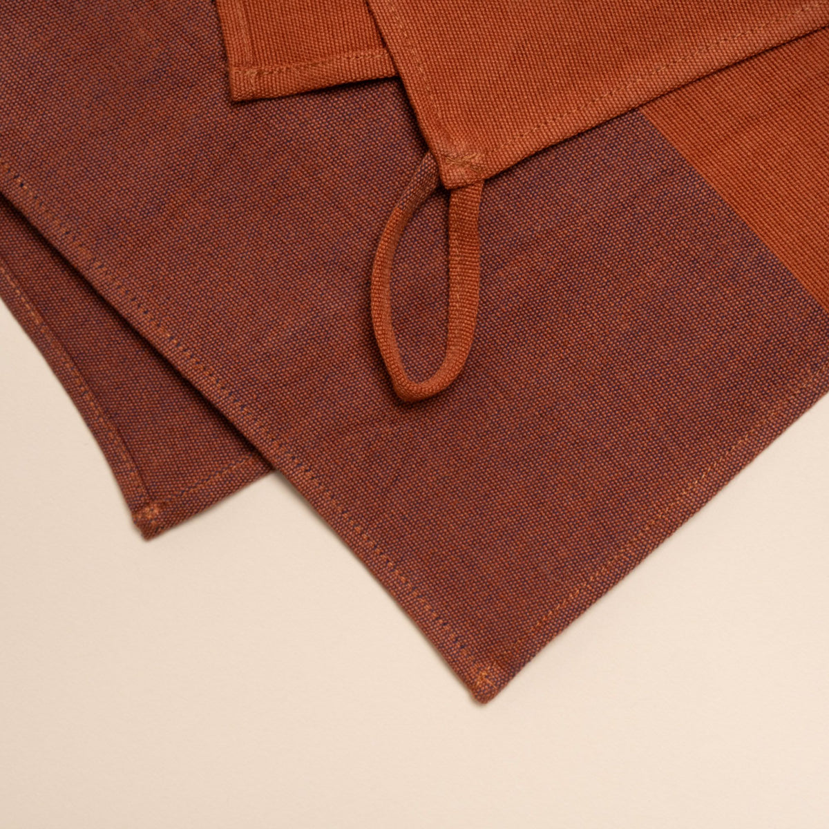 A close up of a folded tea towel with color blocks of rust and dark red, and featuring a hanging loop on a corner