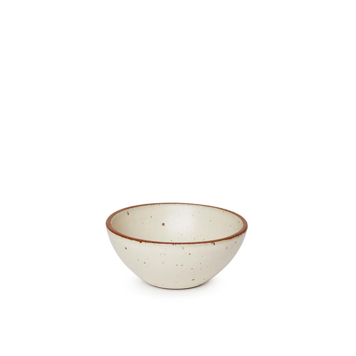 A small dessert sized rounded ceramic bowl in a warm, tan-toned, off-white color featuring iron speckles and an unglazed rim