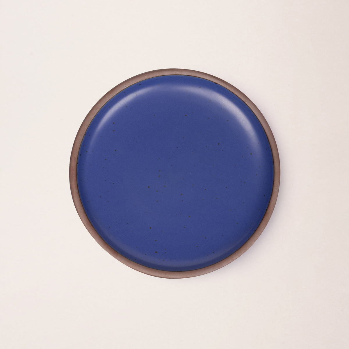 A dinner sized ceramic plate in a cobalt blue color featuring iron speckles and an unglazed rim