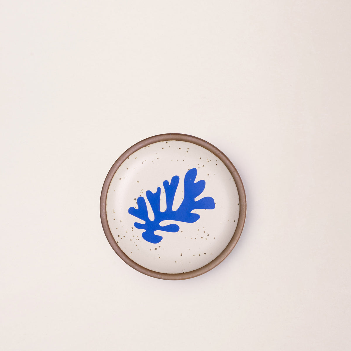 A ceramic dessert sized plates in a warm off-white color with unglazed rim, a frond-like cut-outs from Henri Matisse’s La Perruche et la sirène.