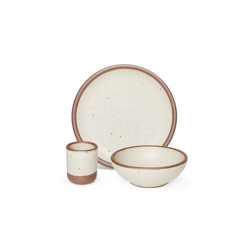 A small tiny cup, a medium sized plate, and a small breakfast bowl paired together in a warm, tan-toned, off-white color featuring iron speckles.
