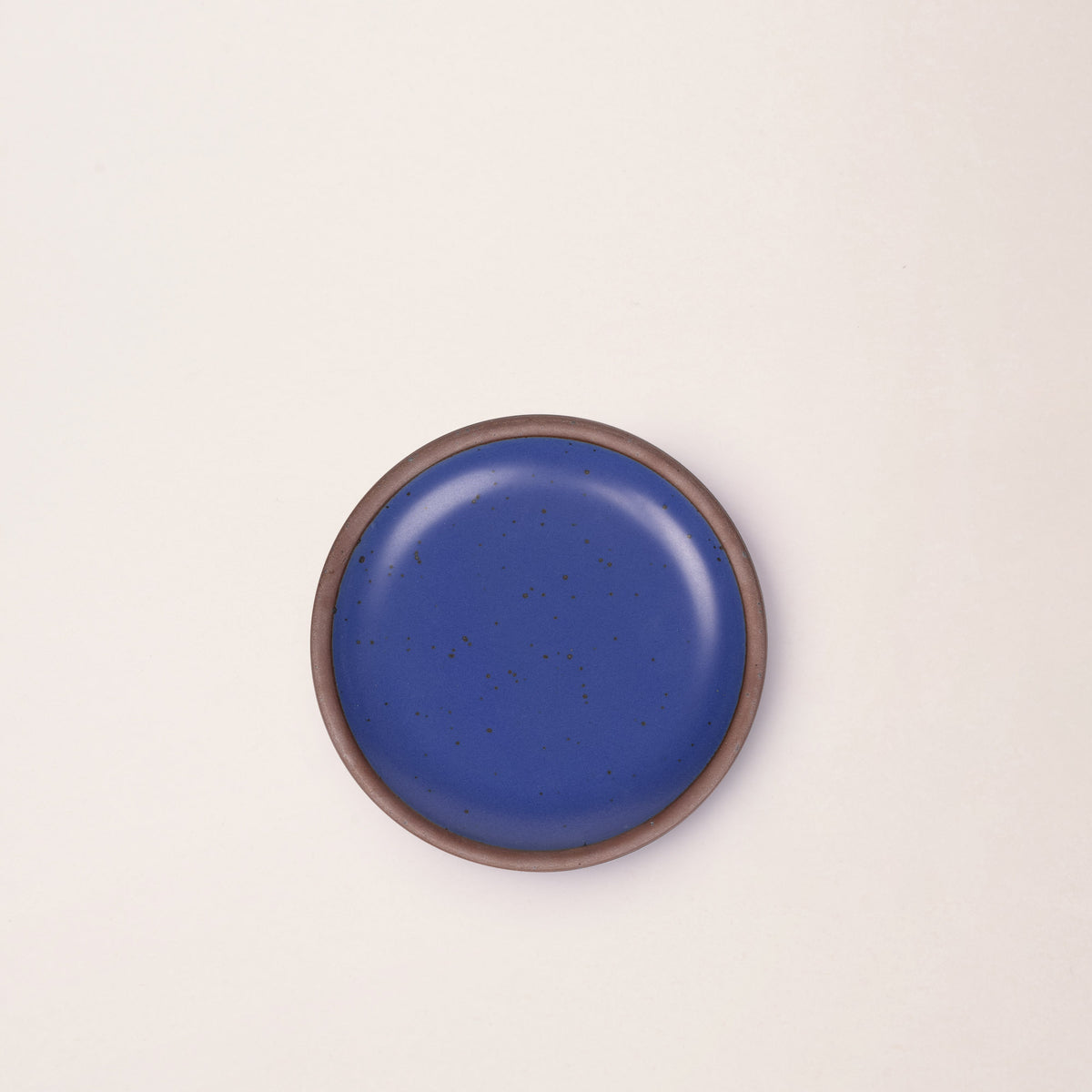 A dessert sized ceramic plate in a cobalt blue color featuring iron speckles and an unglazed rim.
