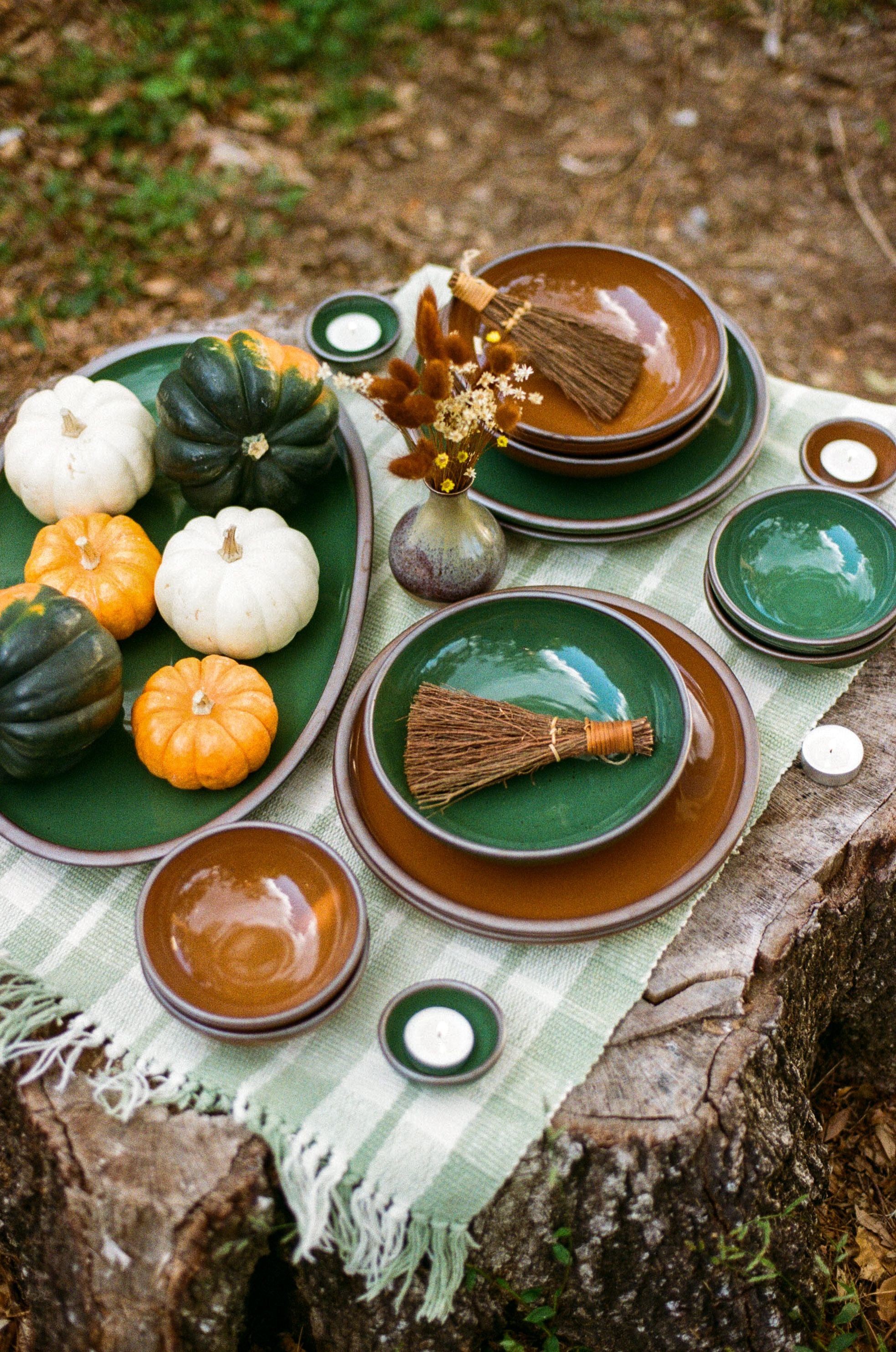 Shiny green and brown pots sit outside on a stump topped with small gourds and dried florals.