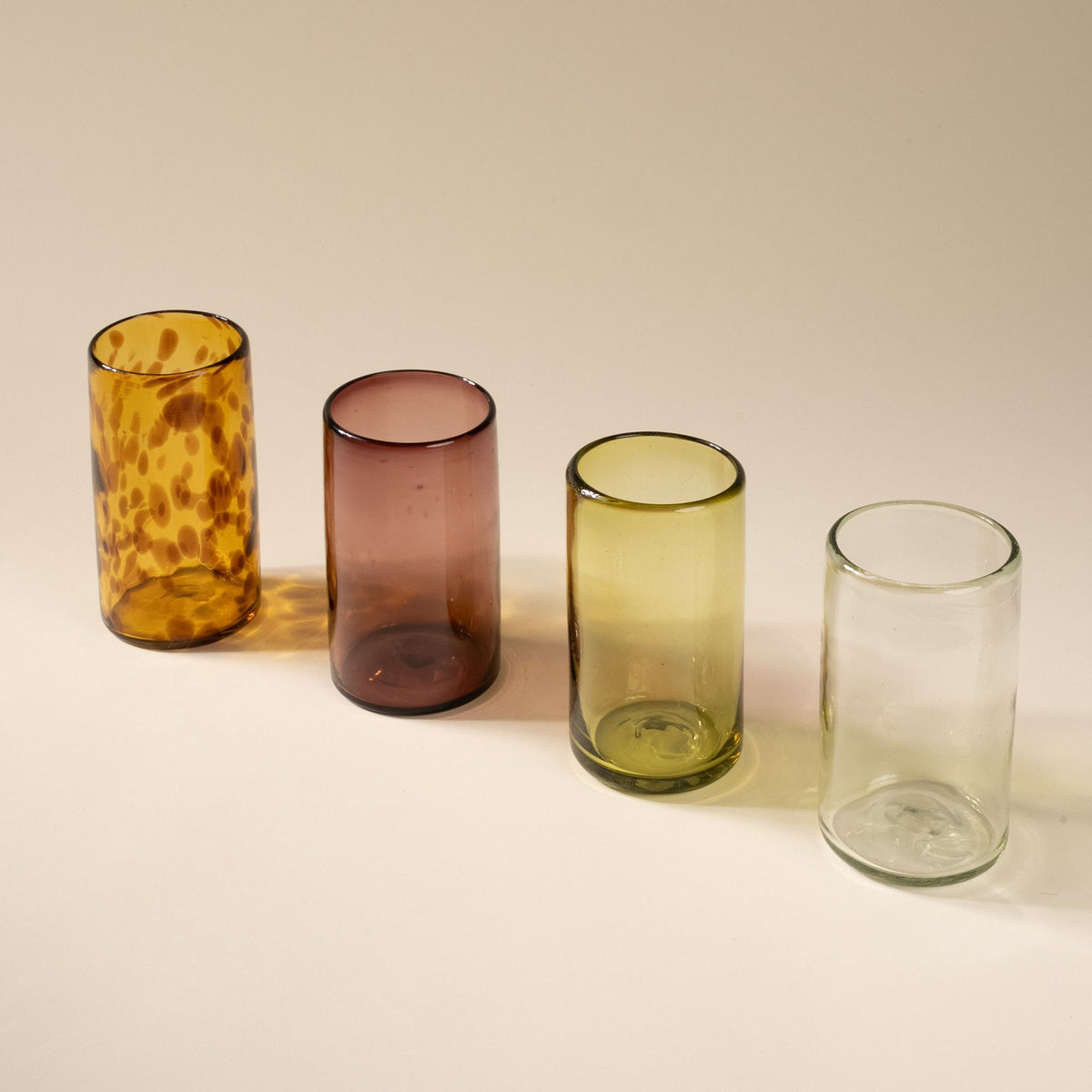A row of tall transparent tumbler glasses in different colors including: tortoiseshell, light plum, olive green, and clear