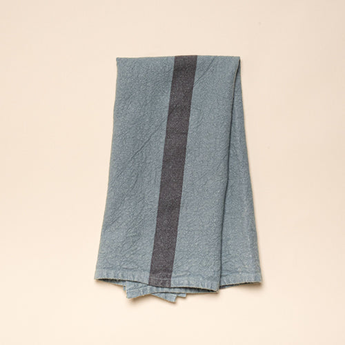 A folded linen towel in a blue-grey color with a dark grey stripe in the middle