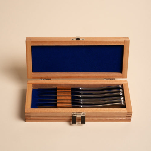Set of six polished steel steak knives in a wooden box lined with deep blue fabric.