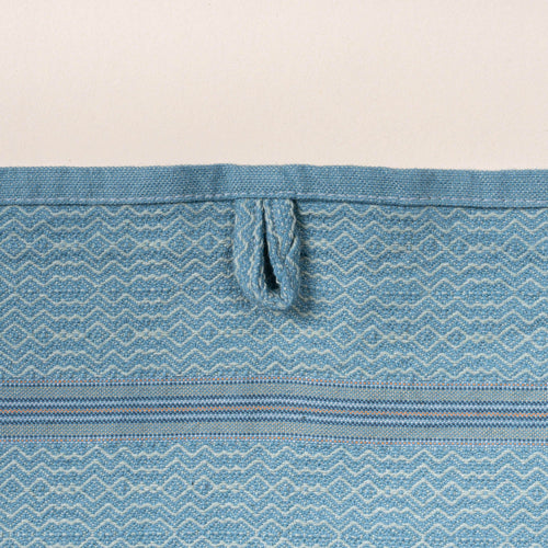 Close-up of a blue woven towel with a zigzag-and-diamond texture, stitched hanging loop, and thin striped band detail.