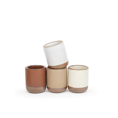 A set of 4 small, short ceramic mug cups in a cool terracotta, warm off-white, cool white, and warm pale brown colors featuring iron speckles and unglazed rim