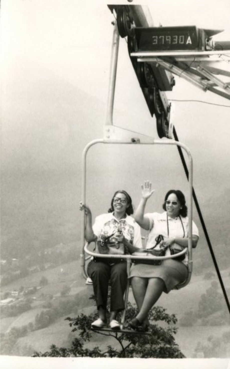 two women in a ski lift in summer clothes overlooking a city