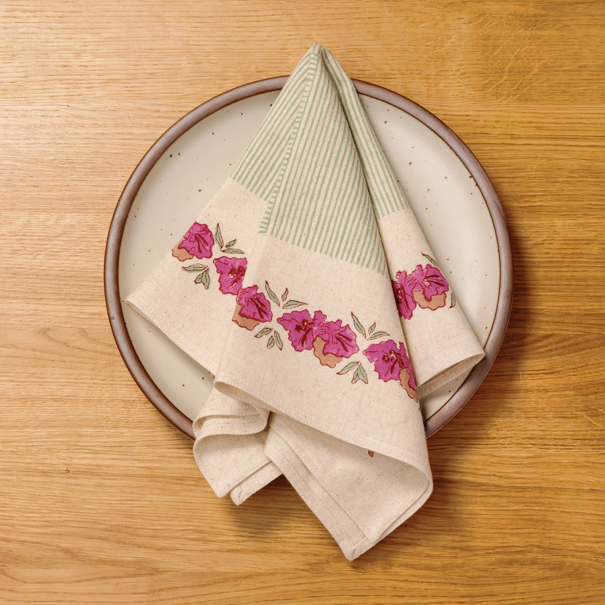 Floral and green-striped linen napkin folded on a speckled ceramic dinner plate on a wooden table.