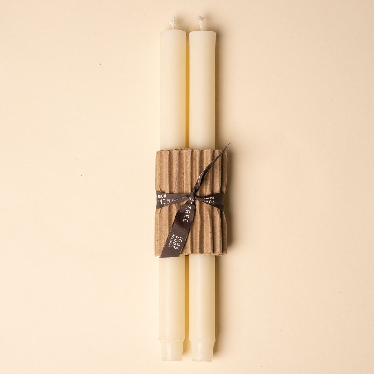Two ivory taper candles bundled with corrugated cardboard and tied with a black ribbon on a neutral background.