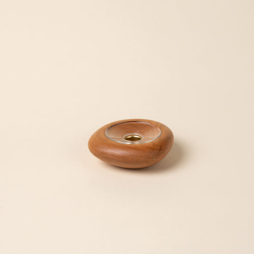 Small round cherry wood candle holder with visible grain and a glass insert in the center, displayed against a neutral background.