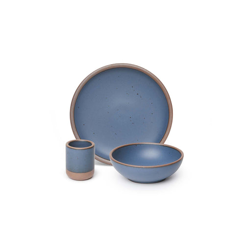 A small tiny cup, a medium sized plate, and a small breakfast bowl paired together in a cool, medium blue color featuring iron speckles.