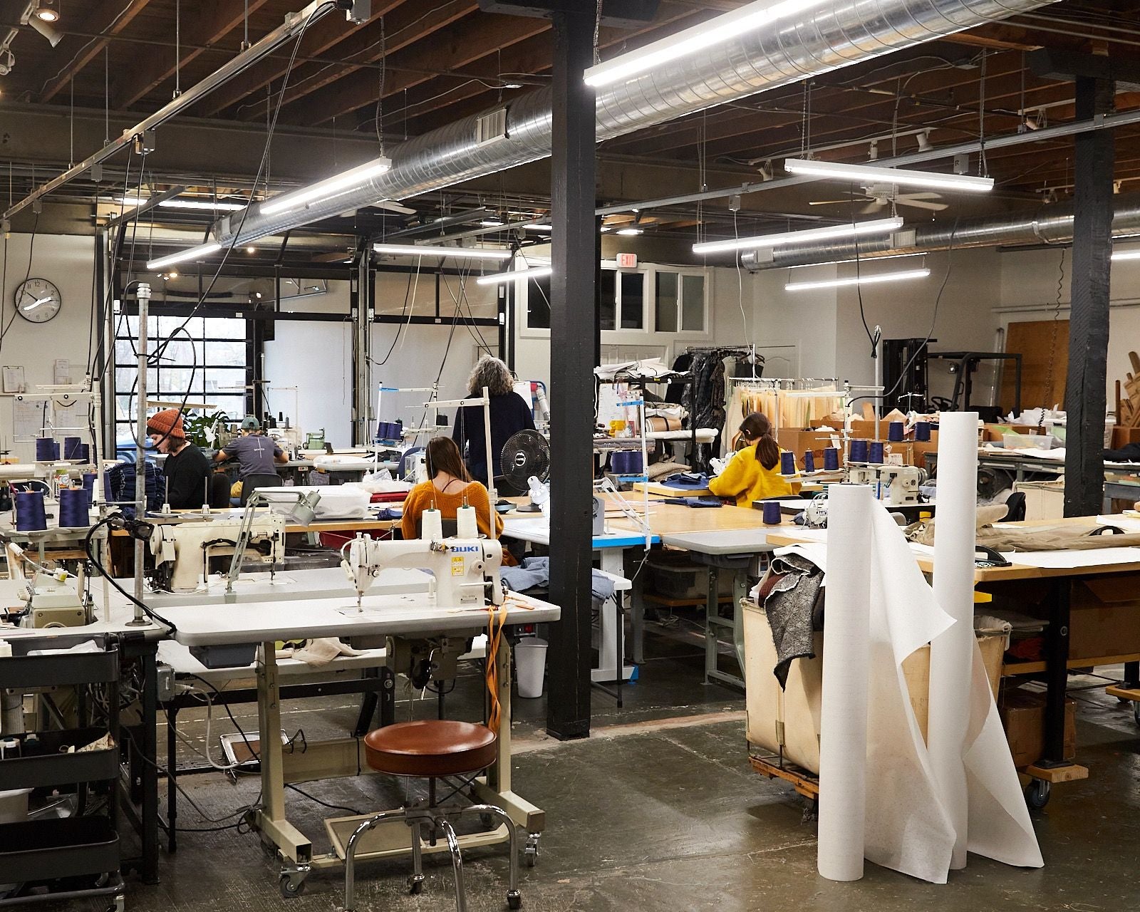 Inside a large sewing studio with several desks and sewing machines set up with people working at them.