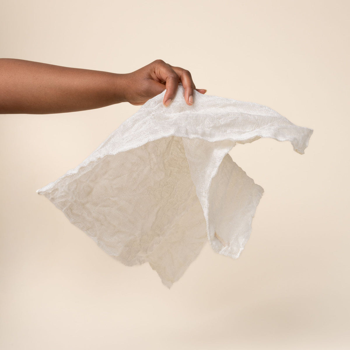 Hand holding a rigid and dry natural linen cleaning cloth showing a subtle woven texture and stitched edges.