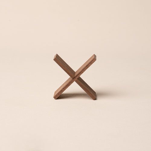 Small wooden X-shaped stand made of two intersecting pieces, displayed on a beige background.