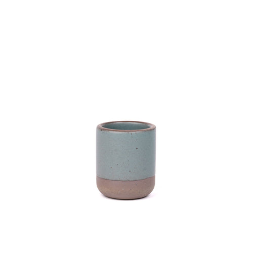 A small, short ceramic mug cup in a blue-grey color with an unglazed rim and iron speckles