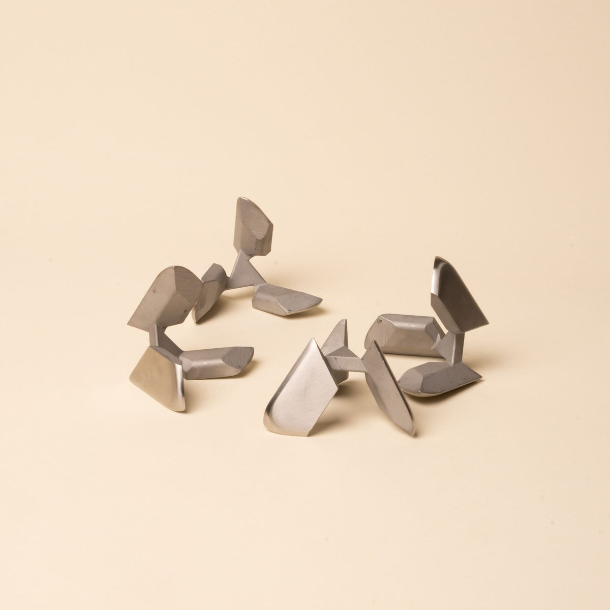Disassembled silver metal tetra puzzle pieces arranged loosely on a neutral surface.