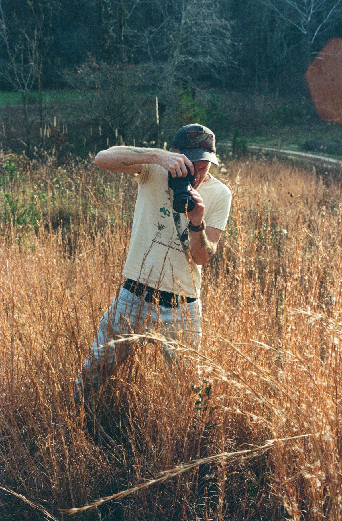 A man standing outside in tall grass holding a camera