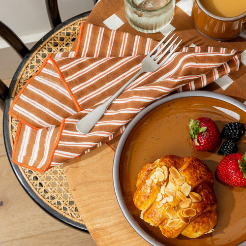 A breakfast scene with a striped cloth napkin and fork on a woven chair, next to a plate holding a croissant topped with almonds and fresh berries.