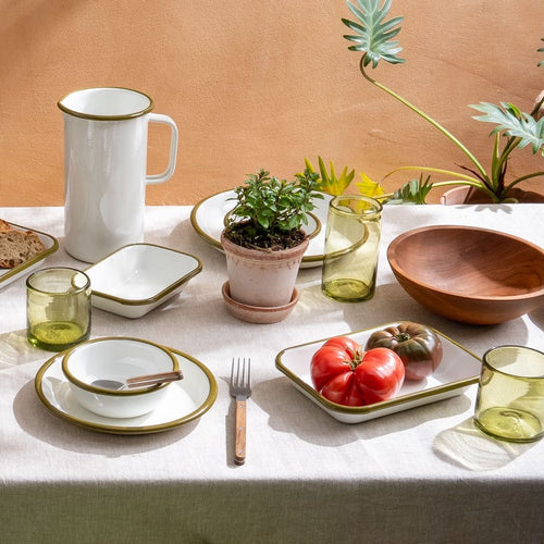 A table filled with white enamel dishes, plates, bowls, and a pitcher, with green tumbler glasses, and more.