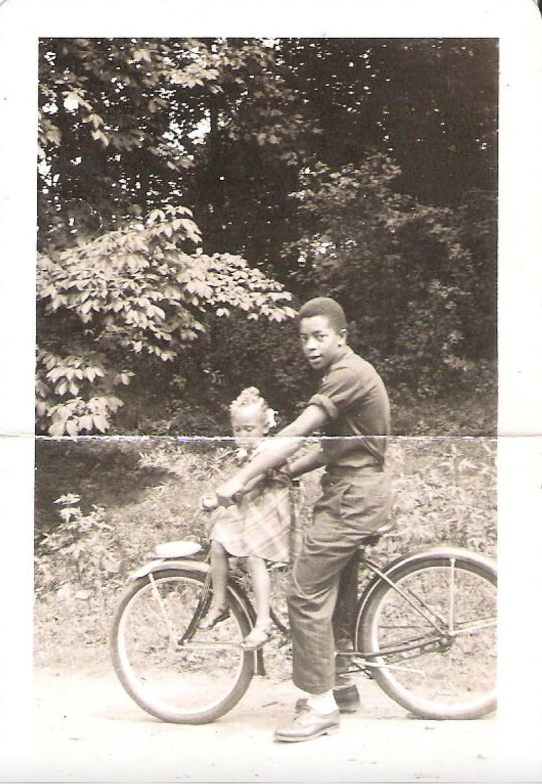 Image of a man on a bicycle with a young girl on the handlebars 