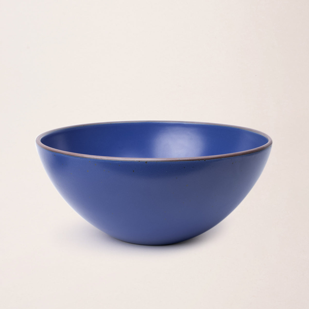 A large ceramic mixing bowl in a cobalt blue color featuring iron speckles and an unglazed rim