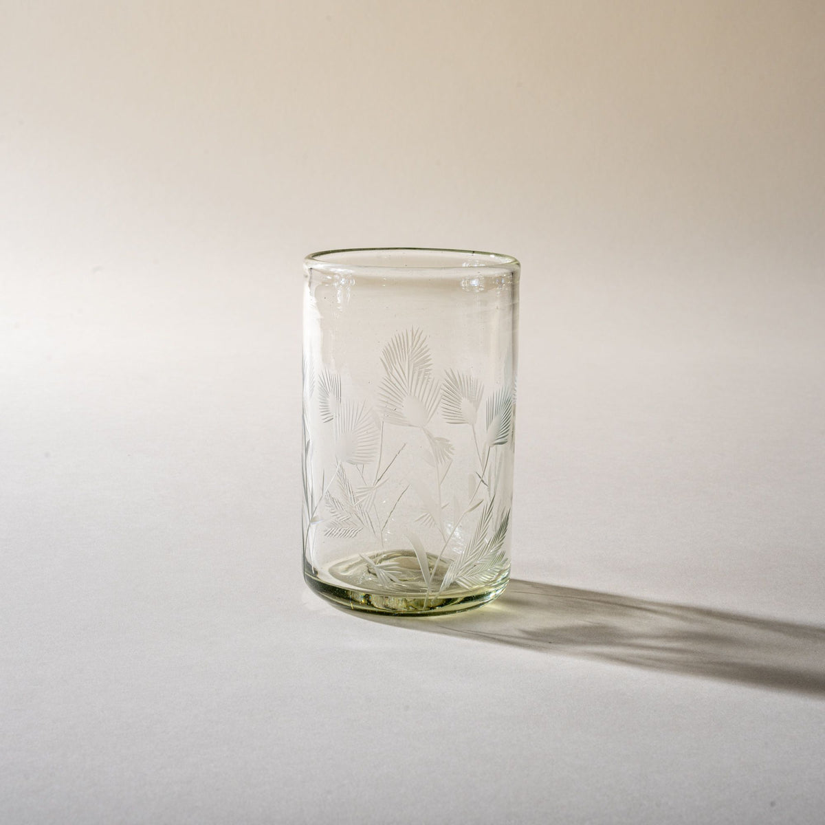 A clear tumbler glass made of recycled glass with etched thistle designs on it