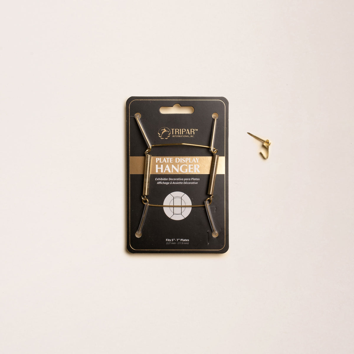 A brass plate hanger in its black cardboard package, with a nail off to the side.