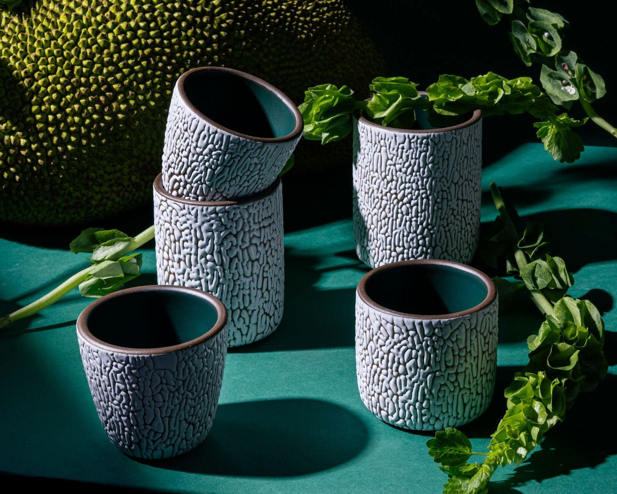 Five white ceramic vessels in various sizes with cracked texture and the interior being dark teal. Artfully arranged in a moody studio setting.