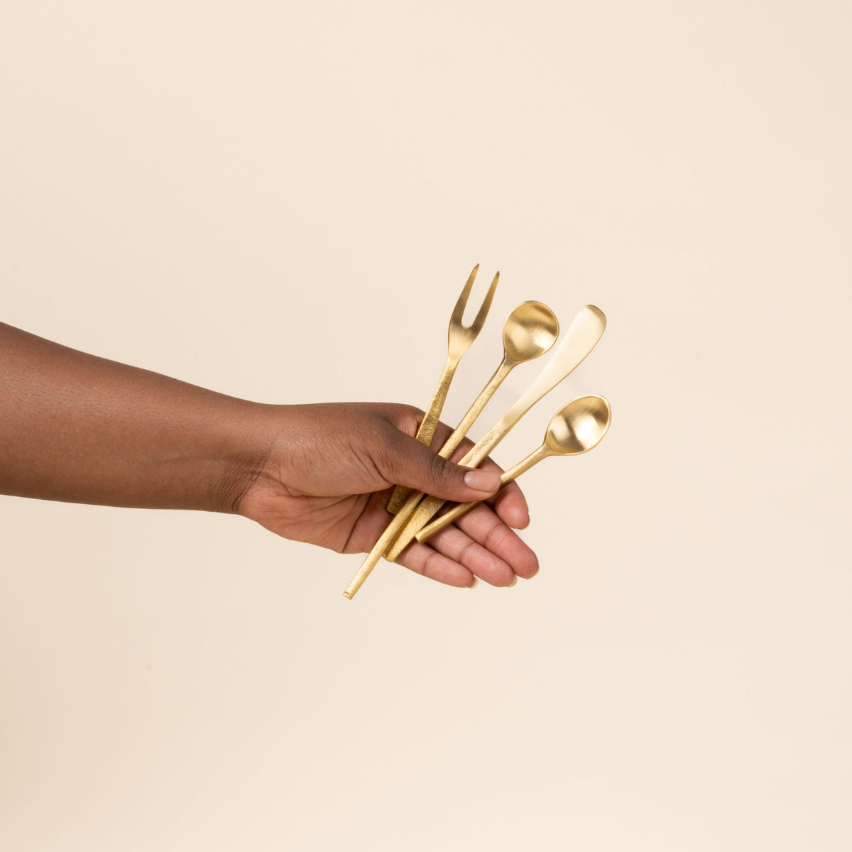 Hand holds out four  brass flatware utensils against a light background