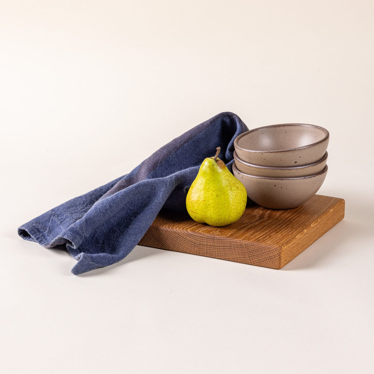 An indigo linen towel with a pair, stack of ceramic bowls, and a small cutting board