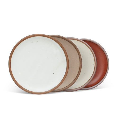 4 medium sized ceramic plates in a cool white, warm pale brown, warm off-white, and cool terracotta colors featuring iron speckles and an unglazed rim.